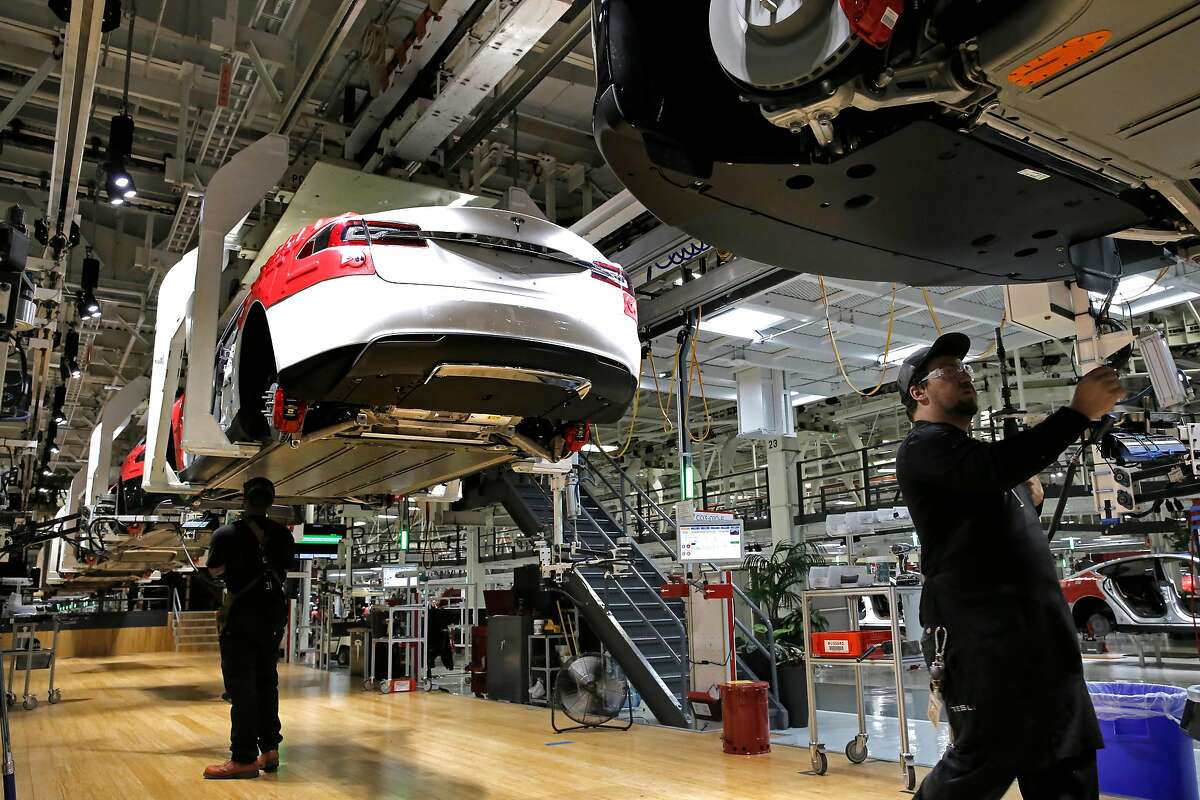Workers under the electric cars as they move through the assembly line at Tesla Motors, California's only full-scale auto manufacturing plant as seen on Thurs. Feb. 19, 2015, in Fremont, Calif.