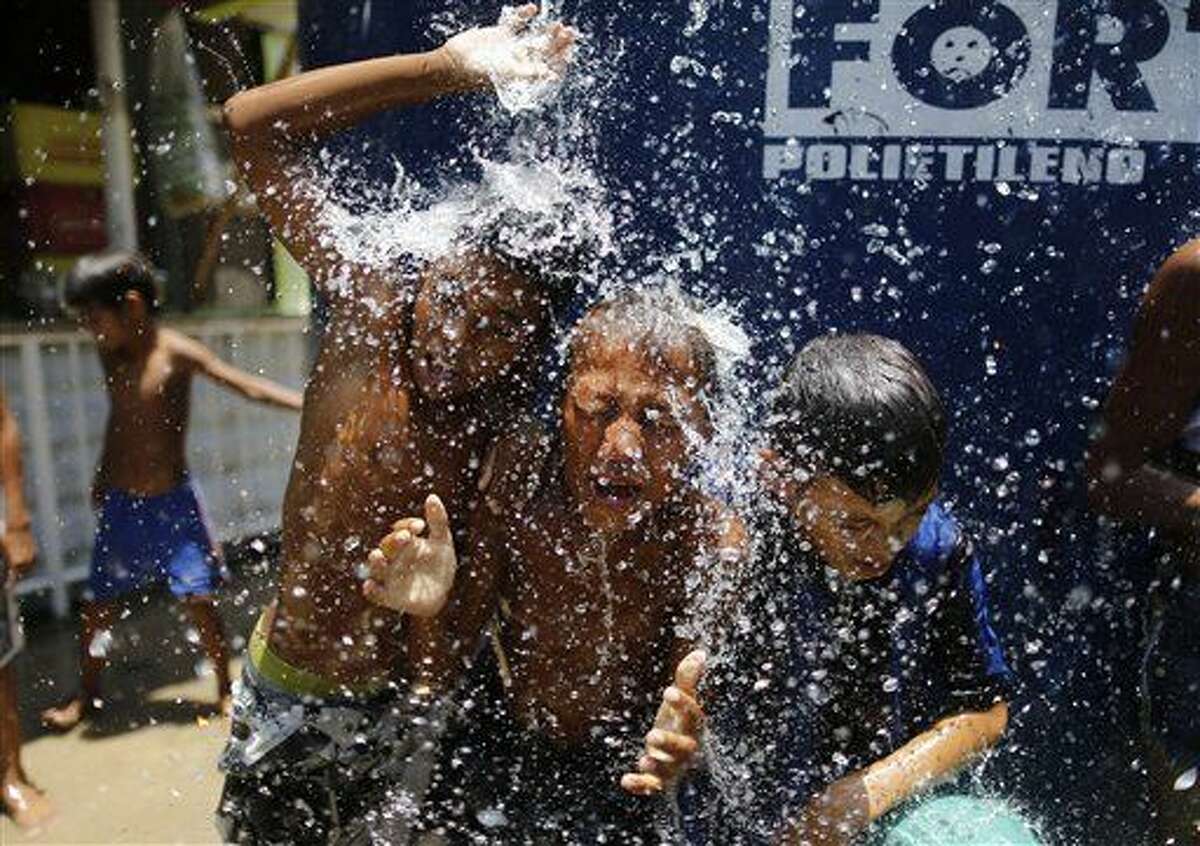 FILE - In this Jan. 29, 2015 file photo, children play under the water that they manage to spill over from a water tank, to cool off from the summer heat, at the Alemao Complex slum in Rio de Janeiro, Brazil. The next day it’s unusually beastly hot, scientists say you can blame three-quarters of it on humans. As climate change gets worse around mid-century, that percentage of extremely hot days being caused by man-made greenhouse gases will push past 95 percent, according to a new study published Monday in the journal Nature Climate Change. (AP Photo/Leo Correa, File)
