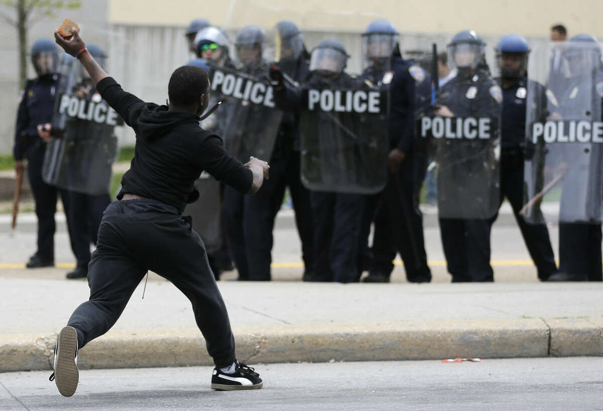 A man throws a brick at police Monday, April 27, 2015, following the funeral of Freddie Gray in Baltimore. Gray died from spinal injuries about a week after he was arrested and transported in a Baltimore Police Department van. (AP Photo/Patrick Semansky)