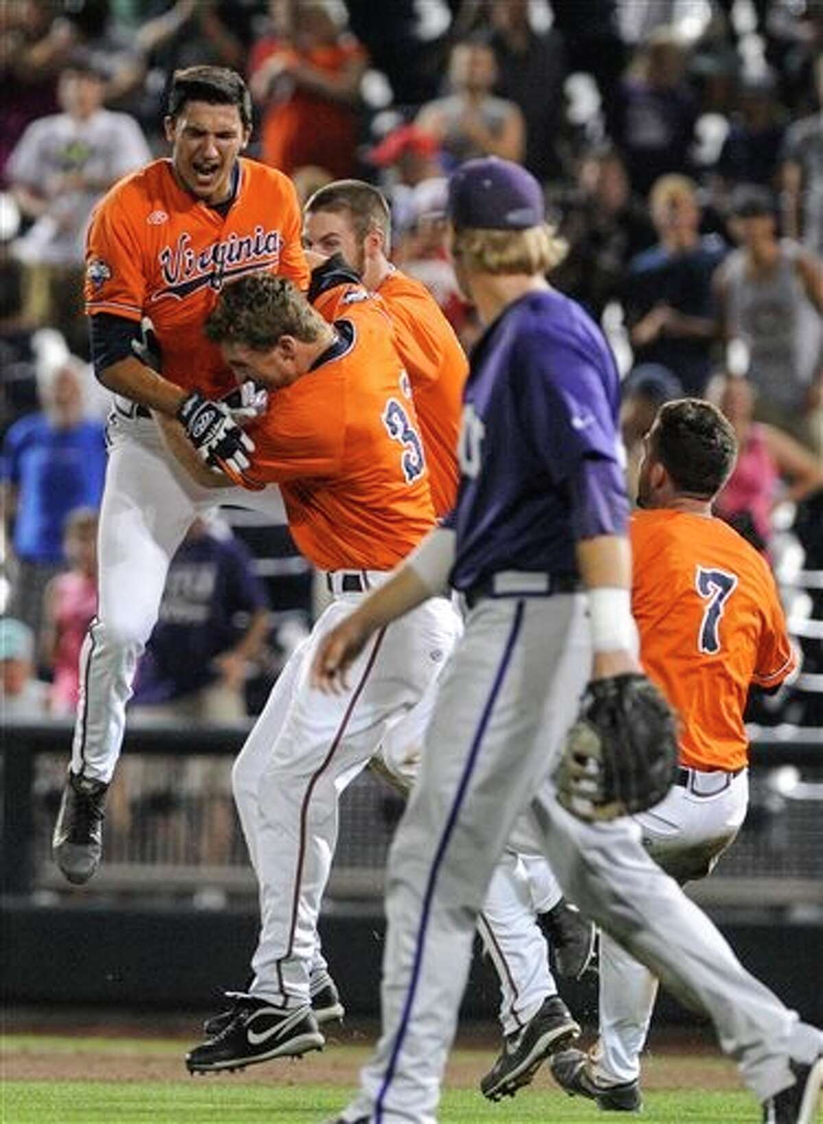 Virginia shortstop Daniel Pinero, left, celebrates with Thomas Woodruff (37) and others after winning 3-2 an NCAA baseball College World Series game against TCU in 15 innings in Omaha, Neb., Wednesday, June 18, 2014. TCU's Kevin Cron is looking on in the foreground. (AP Photo/Eric Francis)