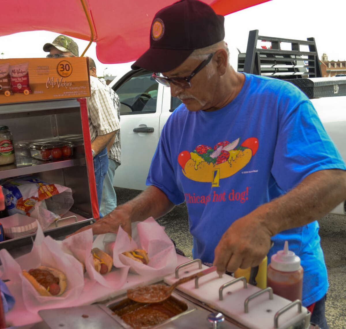 Ric Beltran, who owns and runs Dogmatic hot dog stand from his VW bus, serves up hotgogs with chilli and cheese Wednesday afternoon in Midland. Tim Fischer\Reporter-Telegram