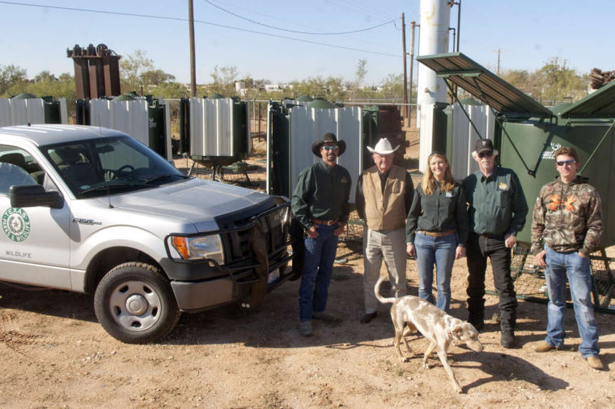 Mule Deer Foundation members Bobby Builta, co-chairman, Al Mitchell, Ret. Texas Ranger, Annaliese Scoggin of Texas Parks & Wildlife, Grier Brunson, co-chairman, and Greg Tomlin, advertising chairman, pose for a group photo with twelve 500-gallon drinker units that collect rainwater for mule deer to drink. Suzie, a two-year old tracking dog