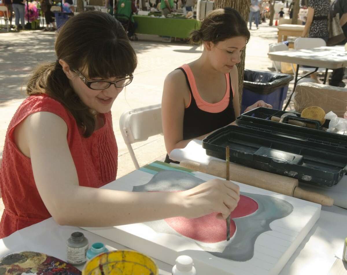 Molly Swanson works on a painting as Danielle Kiser works on a clay piece Saturday at their booth, the Flying Olive, at Celebration of the Arts. The women are among a group of young artists who find inspiration in Midland.