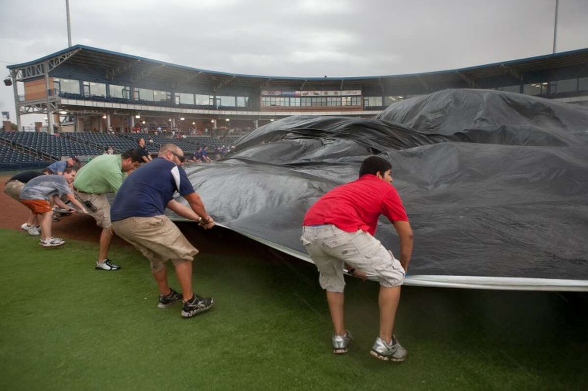 Members of the RockHounds staff battle the wind as they try to lay a tarp over the infield to protect it from the rain Thursday at Citibank Ballpark. The RockHounds will play the Tulsa Drillers in a doubleheader today to make up Thursday's game that was canceled because of the weather.