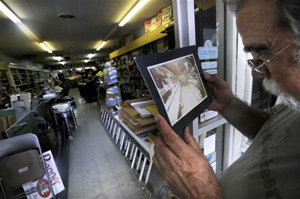 In this Aug. 23, 2013 photo, Joe Pete Forcher compares a 100-year-old photo of Dean Rexall Drug to the way the interior currently looks in Cisco, Texas. Although the store closed in 1999, an estate sale during last weekend of August will allow the public to see decades worth of patent medicines, old cameras and an X-ray machine. (AP Photo/The Abilene Reporter-News, Ronald W. Erdrich)