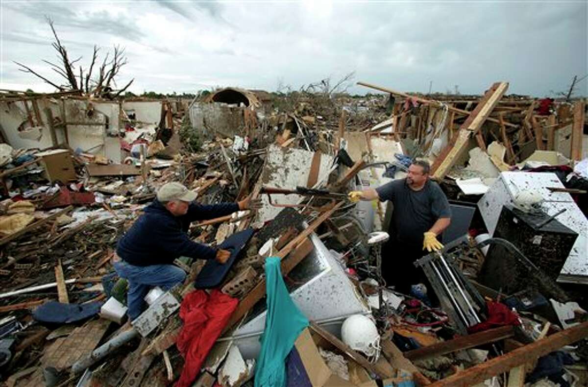 Dalton Sprading, right, hands a gun to his uncle Roger Craft as he salvages items from his tornado-ravaged home Tuesday, May 21, 2013, in Moore, Okla. A huge tornado roared through the Oklahoma City suburb Monday, flattening an entire neighborhoods and destroying an elementary school with a direct blow as children and teachers huddled against winds. (AP Photo/Charlie Riedel)