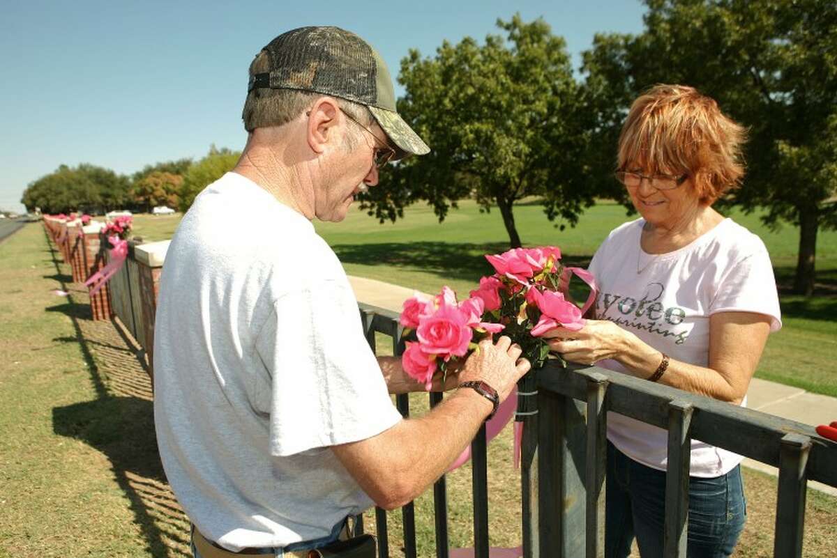 Cherrie Wilson, a breast cancer survivor, and her husband Jim decorate the fence along Grafa Park with pink flowers and bows to help raise awareness. Cindeka Nealy/Reporter-Telegram