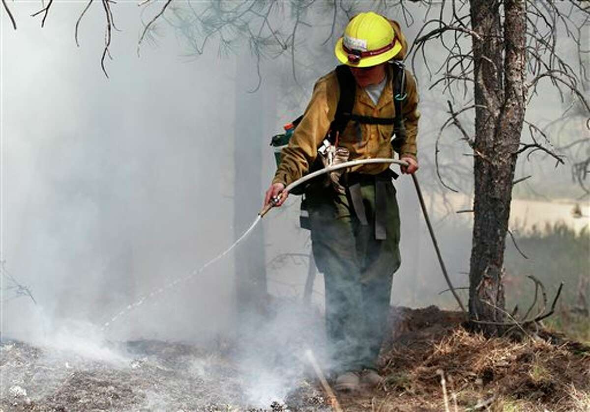 An AmeriCorps volunteer firefighter assigned to the El Paso County Sheriff's Office sprays water to contain a spot fire in an evacuated area of residences, forest, and ranches in the Black Forest wildfire area, north of Colorado Springs, Colo., on Thursday, June 13, 2013. The blaze in the Black Forest is now the most destructive in Colorado history, surpassing last year's Waldo Canyon fire, which burned 347 homes, killed two people and led to $353 million in insurance claims. (AP Photo/Brennan Linsley)