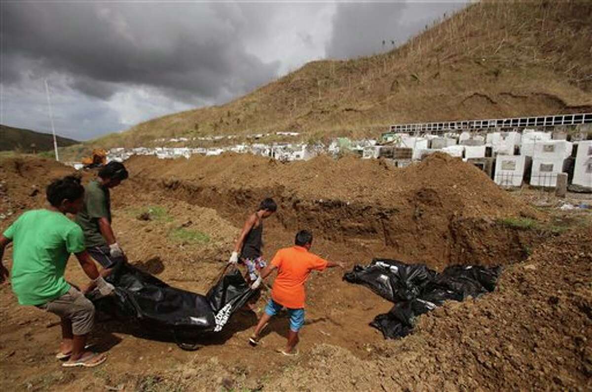 Workers start to arrange body bags at a mass burial site at the Basper public cemetery in Tacloban, Leyte province, central Philippines on Thursday, Nov. 14, 2013. Workers in the typhoon-shattered city buried 100 of its thousands of dead in a hillside mass burial Thursday as desperately needed aid began to reach some of the half-million people displaced by the disaster. (AP Photo/Aaron Favila)