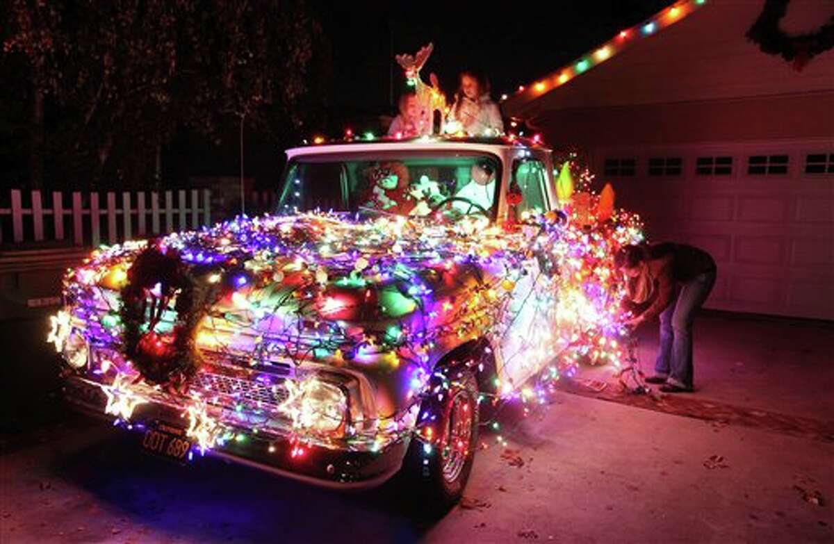 In this Sunday Dec. 9, 2012 photo, Adriana Leiss and her daughters Gabriella and Amelia replace burned out light bulbs on their 1965 Chevy pick-up truck decorated for Christmas at their house, on what is known as "Candy Cane Lane" in the Woodland Hills section of Los Angeles. (AP Photo/Richard Vogel)