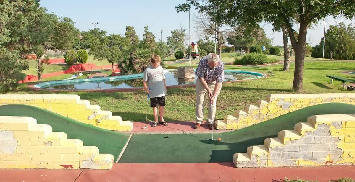 Parker Anderson, 8, left, watches as his grandfather Ralph Arrell take his second shot at getting his ball over the second hill Tuesday during their putt putt golf game at Green Acres Miniature Golf. Cindeka Nealy/ Reporter-Telegram