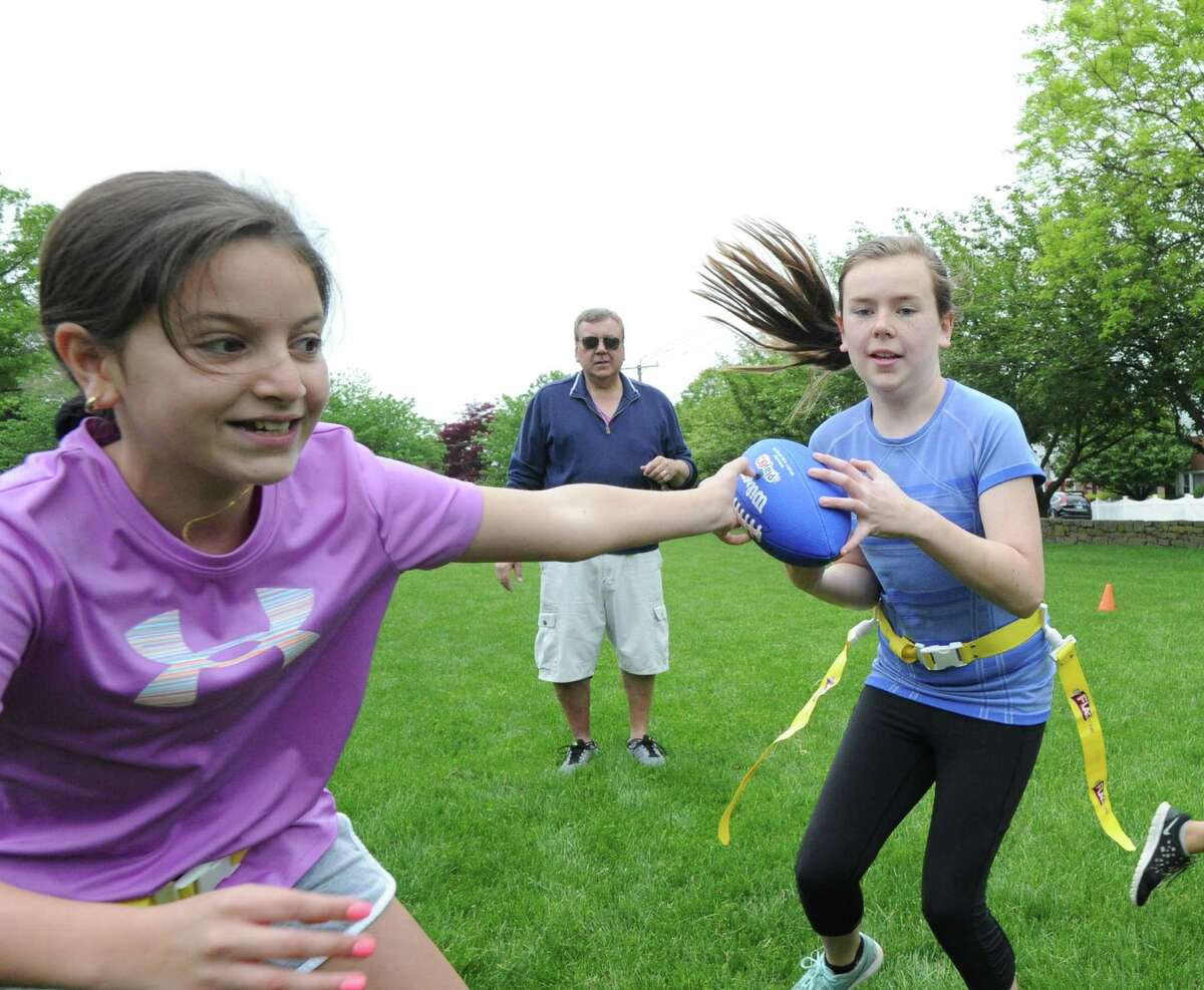 At left, Angel Furano, 12, hands the ball off to teammate Erin Morlock, 12, on a running play during the Chargers flag football practice at Pemberwick Park in the Pemberwick section of Greenwich, Conn., Saturday, May 21, 2016. In the background is Charger coach Jim Morlock.