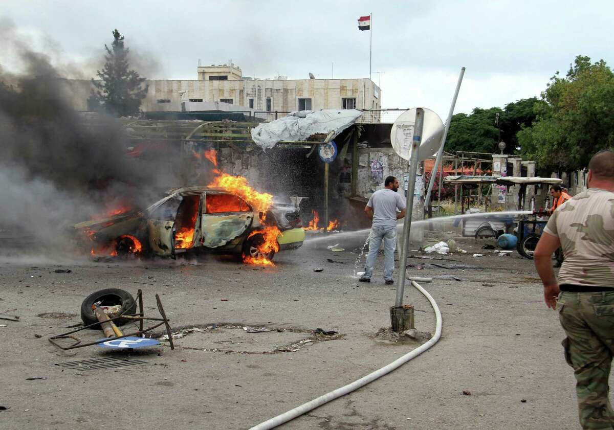 In this photo released by the Syrian official news agency SANA, a firefighter, right, extinguishes a burning car at the scene where suicide bombers blew themselves up, in the coastal towns of Tartus, Syria, Monday, May 23, 2016. Syrian TV said suicide bombers blew themselves followed by a car bomb in a parking lot packed during morning rush hour. (SANA via AP)