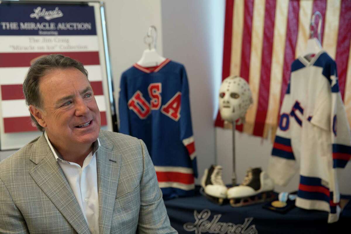 Jim Craig, the hockey goaltender who helped the U.S. win a miraculous gold medal at the 1980 winter Olympics, is framed by a display featuring the jerseys, skates and goalie equipment he wore in the Soviet and Finland games as well as the iconic American flag that was draped over his shoulders after the gold medal win, as he poses for a photo Tuesday, May 24, 2016, in New York. Craig is now auctioning off the items, including his Olympic gold medal. (AP Photo/Mary Altaffer) ORG XMIT: NYMA101