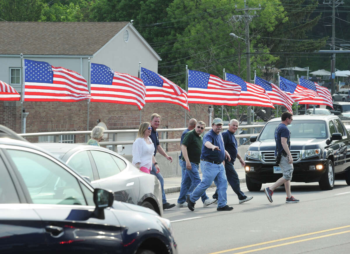 President of the Cos Cob Volunteer Firefighters, Steve Francefort, center, stops traffic to cross the Post Road after he and other volunteers took part in the annual tradition of putting up American flags on the Dave Theis memorial bridge that connects the Greenwich communities of Cos Cob and Riverside, Conn., Thursday, May 26, 2016. Francefort, one of the organizers of the event, said the 20 flags that were placed on the bridge were donated by Greenwich residents, husband and wife, Joe and Barbara Havranek.