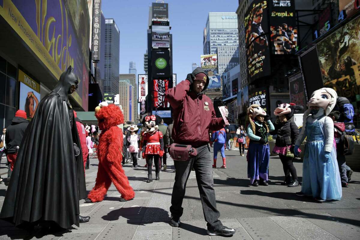 FILE - In this March 29, 2016 file photo, a bus tour ticket seller, center, walks through a group of costumed characters in Times Square in New York. New York City workers have started painting teal rectangles in pedestrian plazas designating where costumed characters can pose with tourists in Times Square. Starting June 21, street performers and costumed characters will be restricted to those areas when soliciting tips from tourists. (AP Photo/Seth Wenig)