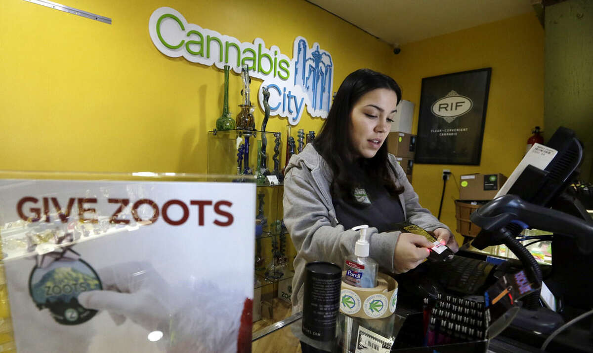 In this Tuesday, Dec. 30, 2014, photo, Cannabis City clerk Jessica Mann scans a customer's ID as she rings up a purchase of marijuana at the shop in Seattle. A year into the nation’s experiment with legal, taxed marijuana sales, Washington and Colorado find themselves with a cautionary tale for Oregon, Alaska or other states that might follow suit: They’re wrestling not with the federal interference many initially feared, but with competition from their own medical marijuana systems or even outright black market sales. (AP Photo/Elaine Thompson)