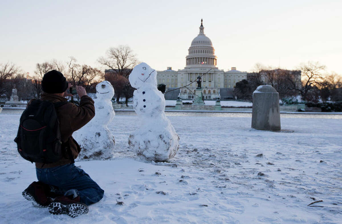 A man takes photos of snowmen with the Capitol in the background, Friday, Jan. 3, 2014, in Washington. After a storm blew through the Washington region overnight, roads are being cleared and many schools systems are closed. The federal government and the District of Columbia government will be open Friday, but workers have the option to take leave or telework. (AP Photo/ Evan Vucci)
