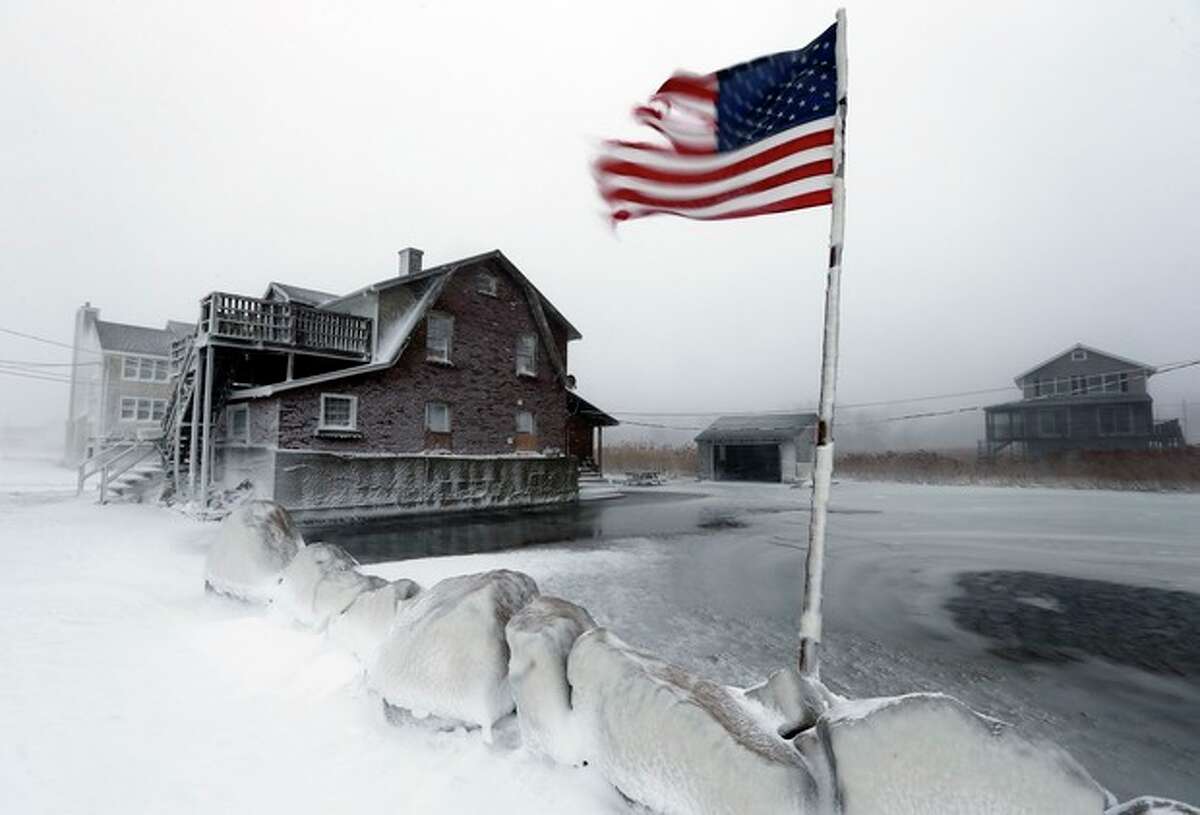 A tattered flag flies by a flooded yard along the shore in Scituate, Mass., Friday, Jan. 3, 2014. A blustering winter storm that dropped nearly 2 feet of snow just north of Boston, shut down major highways in New York and Pennsylvania and forced U.S. airlines to cancel thousands of flights nationwide menaced the Northeast on Friday with howling winds and frigid temperatures. (AP Photo/Michael Dwyer)