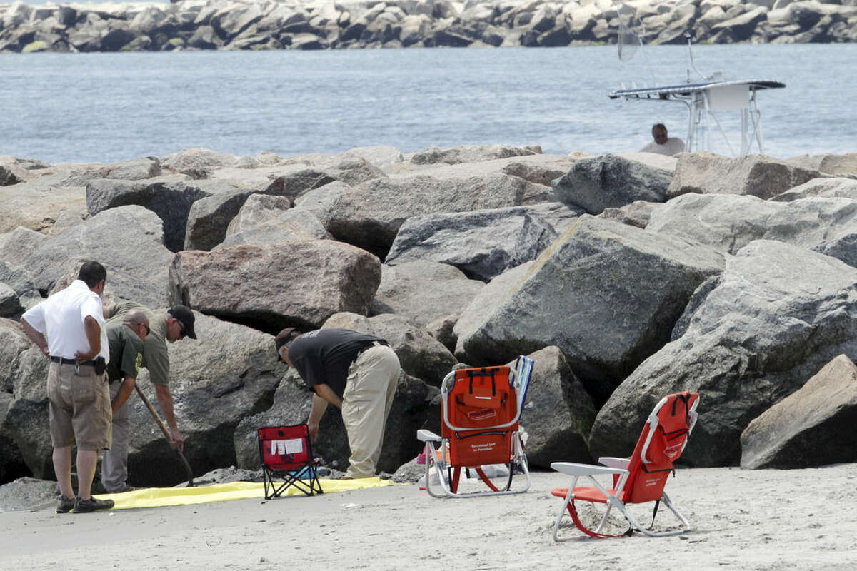 FILE- In this July 11, 2015 file photo, authorities investigate a blast that threw a beachgoer into a nearby jetty at Salty Brine beach in Narragansett, R.I. Scientists determined that the explosion was probably caused by the combustion of hydrogen that had built up around the cable. The U.S. Coast Guard said there are 47 sites in 12 states where there may be an inactive cable similar to the one that caused the explosion in Rhode Island. Michigan, with 21 potential sites, has the most, according to information released to The Associated Press through an open records request. (Steve Szydlowski/Providence Journal via AP, File)