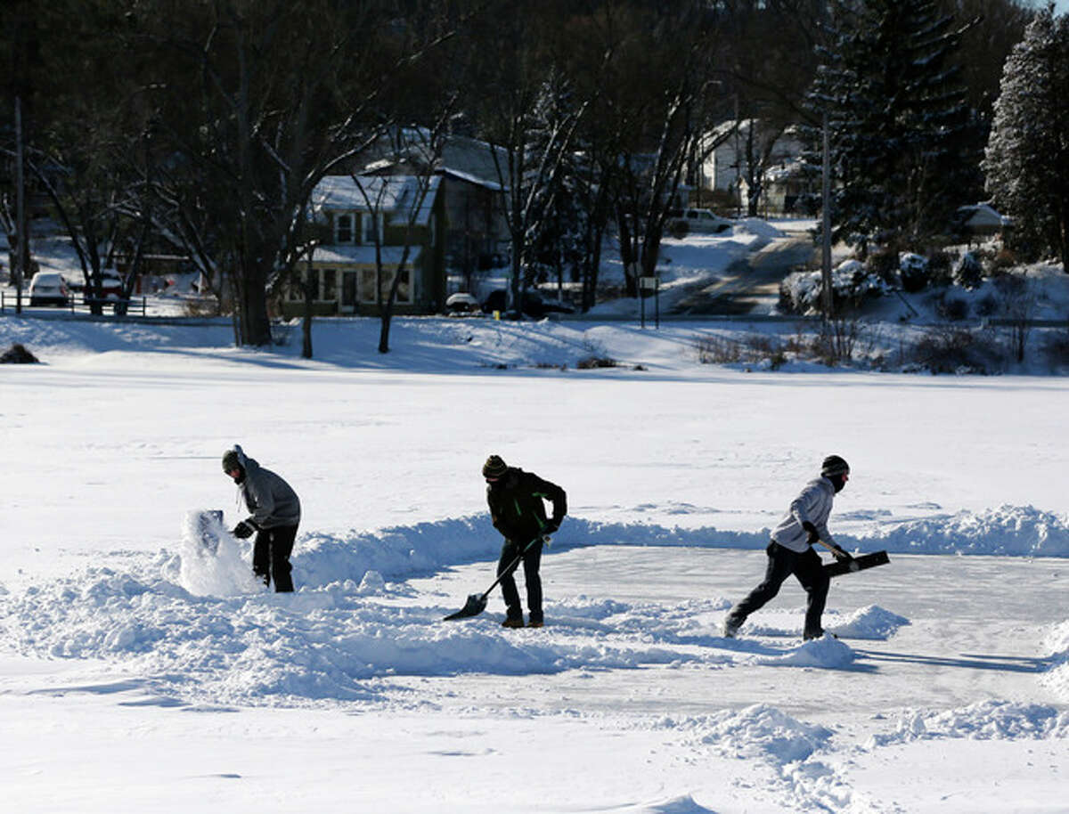 Alex Herrick, Adam Scirico and Peter Herrick clear a section of Hampton Manor Lake to play ice hockey on Friday, Jan. 3, 2014, in East Greenbush, N.Y. Upstate New York on Friday had temperatures in the single digits with below-zero wind chills. (AP Photo/Mike Groll)