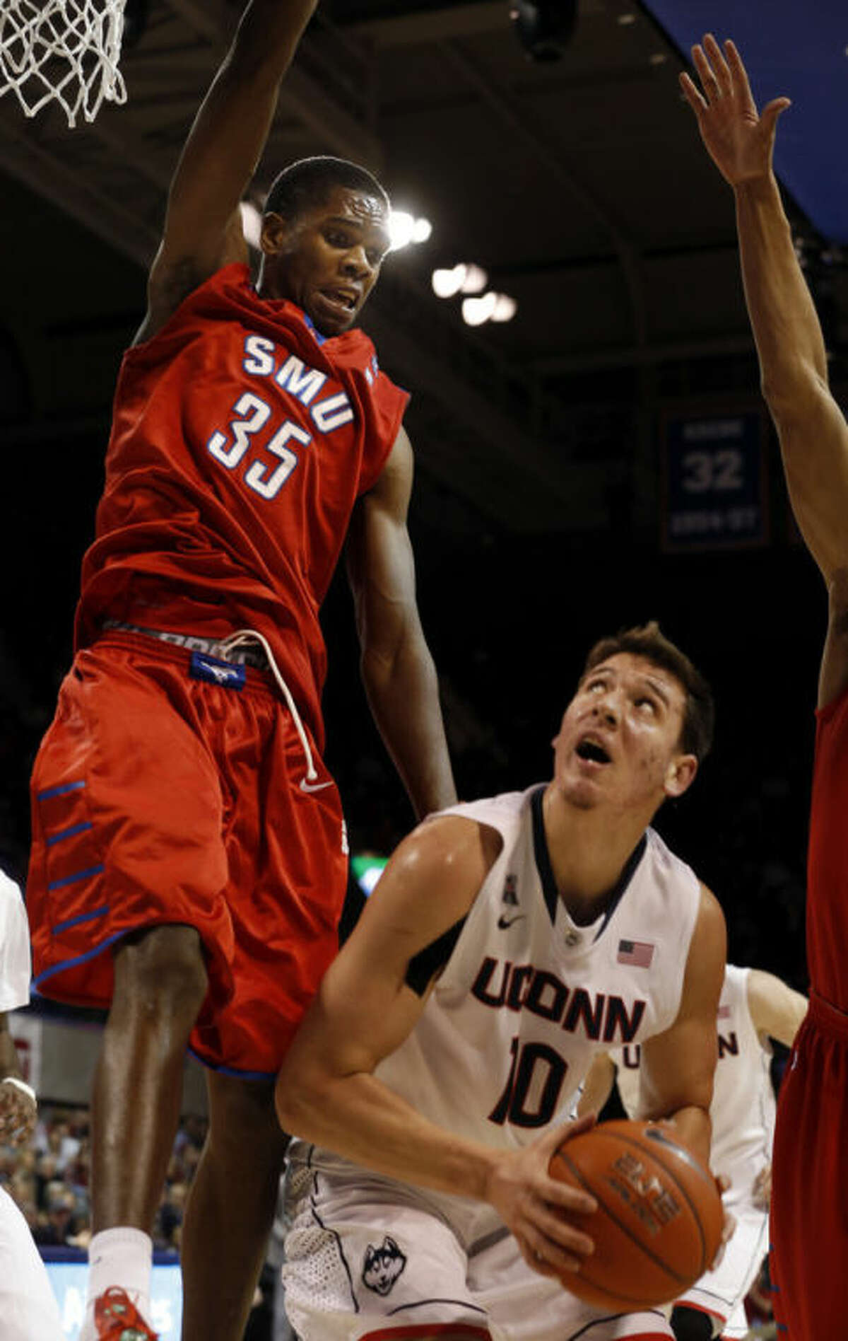 SMU center Yanick Moreira (35) leaps high to try to defend a shot by Connecticut forward Tyler Olander (10) during the first half of a NCAA basketball game on Saturday, Jan. 4, 2014, in Dallas.  (AP Photo/John F. Rhodes)