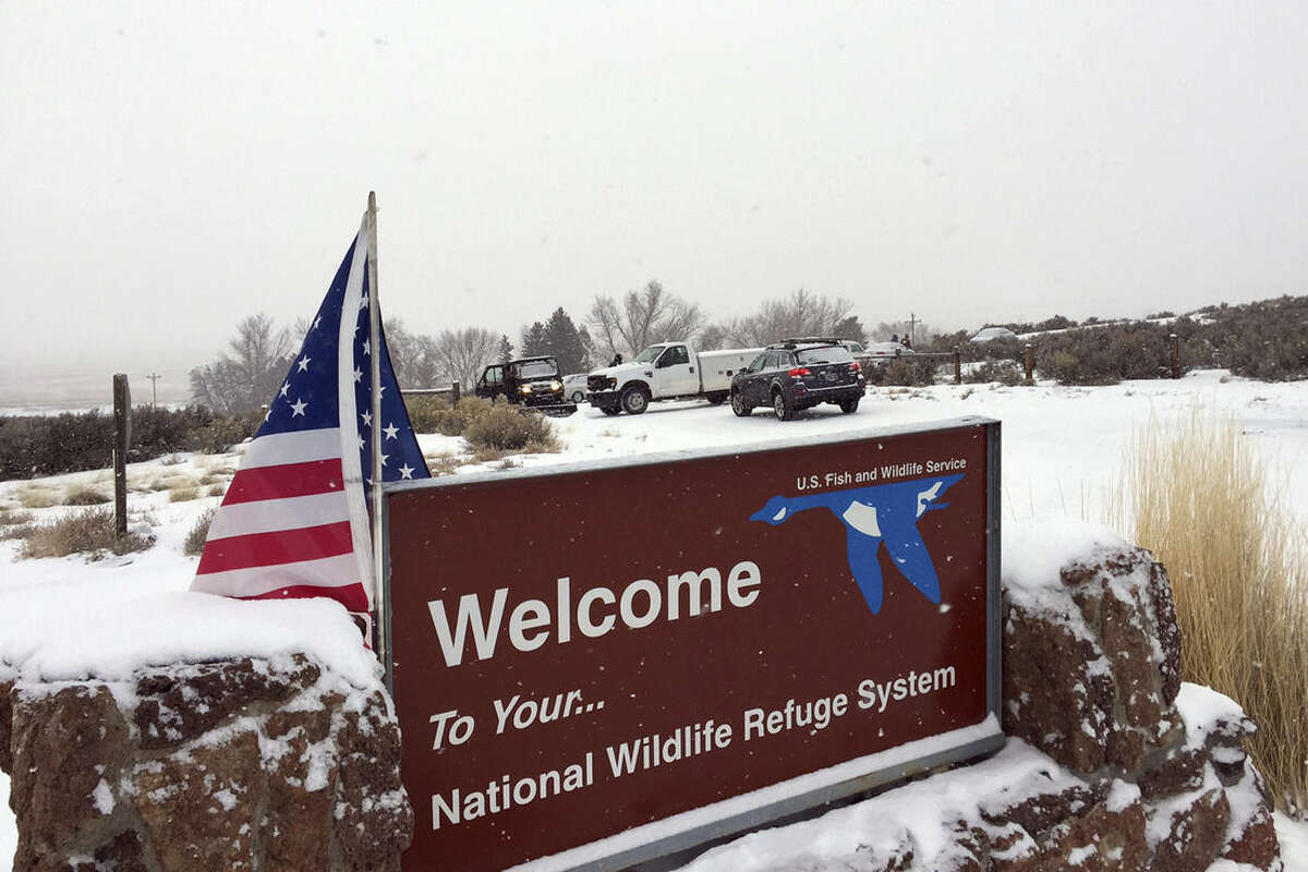 ADDS DETAILS OF SOME VEHICLES SEEN AT THE ENTRANCE - An sign of the National Wildlife Refuge System is seen at an entry of the wildlife refuge, where some vehicles are seen used to block access to the inside of the refuge, about 30 miles southeast of Burns, Ore., Sunday, Jan. 3, 2016. Armed protesters are occupying a building at the national wildlife refuge and asking militia members around the country to join them. The protesters went to Malheur National Wildlife Refuge on Saturday following a peaceful rally in support of two Oregon ranchers facing additional prison time for arson. (Les Zaitz/The Oregonian via AP) MANDATORY CREDIT