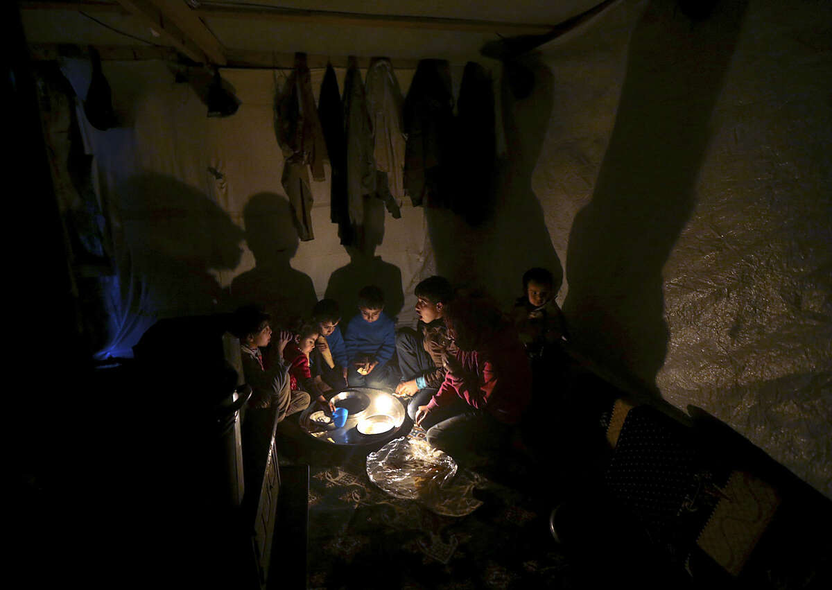 Syrian refugee children sit on the ground inside their tent home as they take their dinner at a Syrian refugee camp, in Deir Zannoun village in the Bekaa valley, eastern Lebanon, on Monday, Jan. 5, 2015. A snow storm is expected to hit Lebanon Monday affecting Syrian refugees, many of whom live in tents without heating. The government estimates there are about 1.5 million Syrians in Lebanon, about one-quarter of the total population. (AP Photo/Hussein Malla)