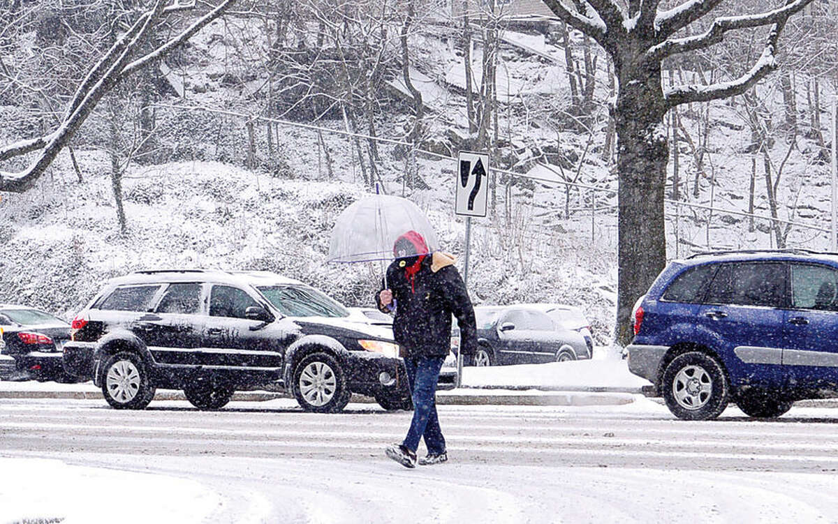 Hour photo / Erik Trautmann A pedestrian crosses Martin Luther King Jr Boulevard during the surprise snowfall Friday morning.