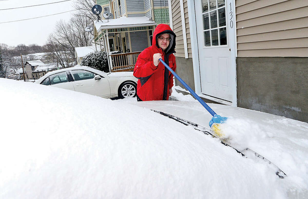 Hour photo / Erik Trautmann Norwalk resident Nick Kiriakidis cleans off his car after the surprise snowfall Friday morning.