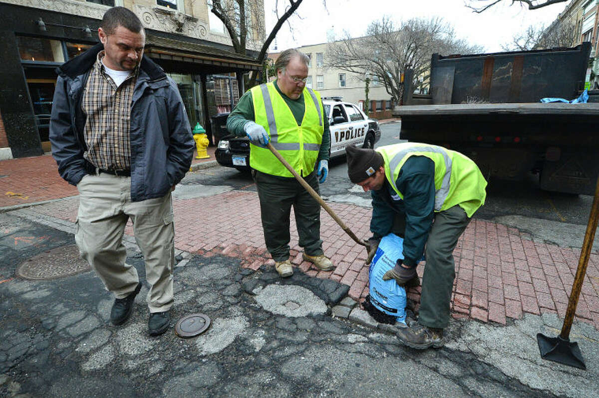 Hour Photo/Alex von Kleydorff Department of Public Works Richard Sirois and John Gardella repair a pothole in a crosswalk on Washington St in SoNo as Road Supervisor Jose Lopez keeps track of the citys potholes and assigns them to road crews