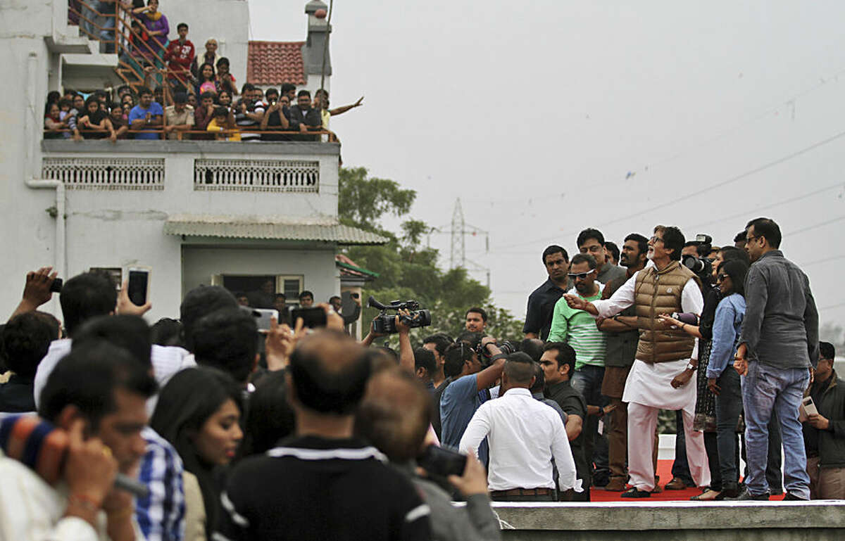 Indians watch as Bollywood actor Amitabh Bachchan, in brown jacket, flies a kite during the kite festival in Ahmadabad, India, Wednesday, Jan. 14, 2015. Bollywood actors Dhanush and Akshra Hasan accompanied Bachchan to promote their upcoming movie "Shamitabh". (AP Photo/Ajit Solanki)