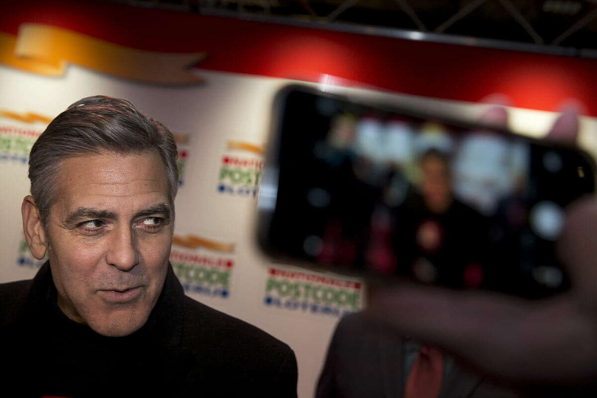 A person takes a picture of U.S. actor George Clooney as he arrives at Carre theater in Amsterdam, Netherlands, Tuesday, Jan. 26, 2016, to attend the Nationale Postcode Loterij's Goed Geld Gala. Sixty-six cultural institutions will receive donations adding up to a total of euro 62.5 million, or $67.8 million. (AP Photo/Peter Dejong)