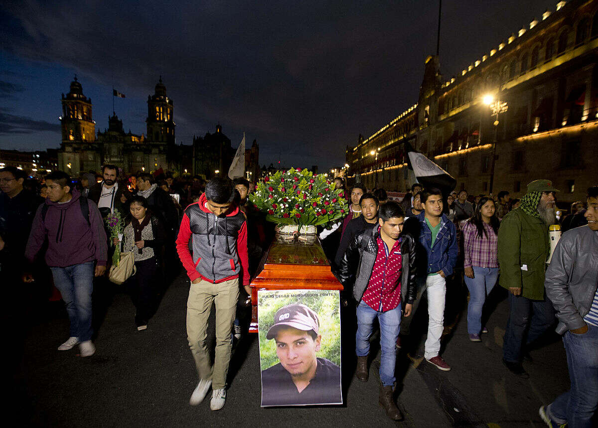 Protestors carry an empty coffin with the image of Julio Cesar Mondragon, who was killed in September 2014 on the same night 43 of his fellow students from a rural teachers college disappeared in the southern state of Guerrero, during a march marking the 16-month anniversary of their disappearance, in Mexico City, Tuesday, Jan. 26, 2016. Mondragon family lawyer Sayuri Herrera is questioning the detention of a man accused killing the Julio Cesar. (AP Photo/Eduardo Verdugo)