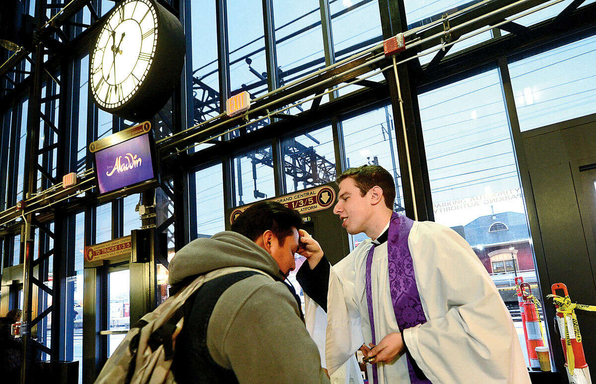 Hour photo / Erik Trautmann St. Paul’s on the Green Reverend Peter Thompson offers Ashes-to-Go to commuters at the South Norwalk train station on Wednesday morning. This was the first year that St. Paul's took part in the 9 year old Episcopal Ashes-to-Go tradition.