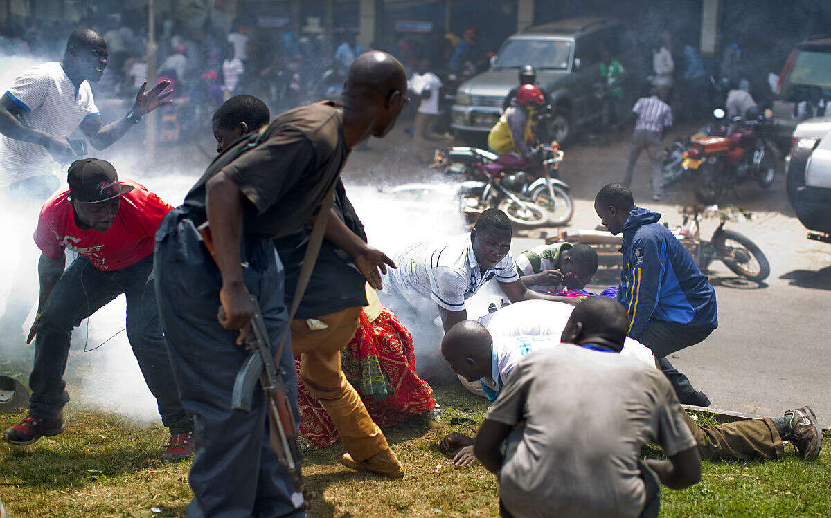 Bodyguards pile on top of leading opposition leader and presidential candidate Kizza Besigye, right in white only showing his back, as riot police fire tear gas at him when he attempted to walk with his supporters along a street in downtown Kampala, Uganda Monday, Feb. 15, 2016. Ugandan riot police arrested Besigye after tear-gassing him and his supporters when they tried to go from one election rally to another. (AP Photo/Ben Curtis)