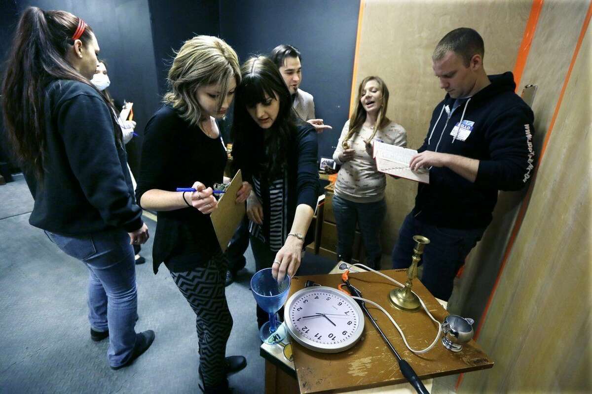 In a photo from Friday, Jan. 23, 2015 in Detroit, Audrey Poe, center left, and Erika Sorensen, center, look over clues in “Trapped in a Room With a Zombie.” Up to a dozen people are locked in a room for an hour alongside a zombie that’s chained to a wall. Every five minutes, a buzzer sounds, and the zombie is given another foot of chain, allowing the undead creature to scamper even closer to its next meal. If participants don’t solve a series of puzzles within the 60 minutes, the zombie “eats” everyone in the group. (AP Photo/Carlos Osorio)