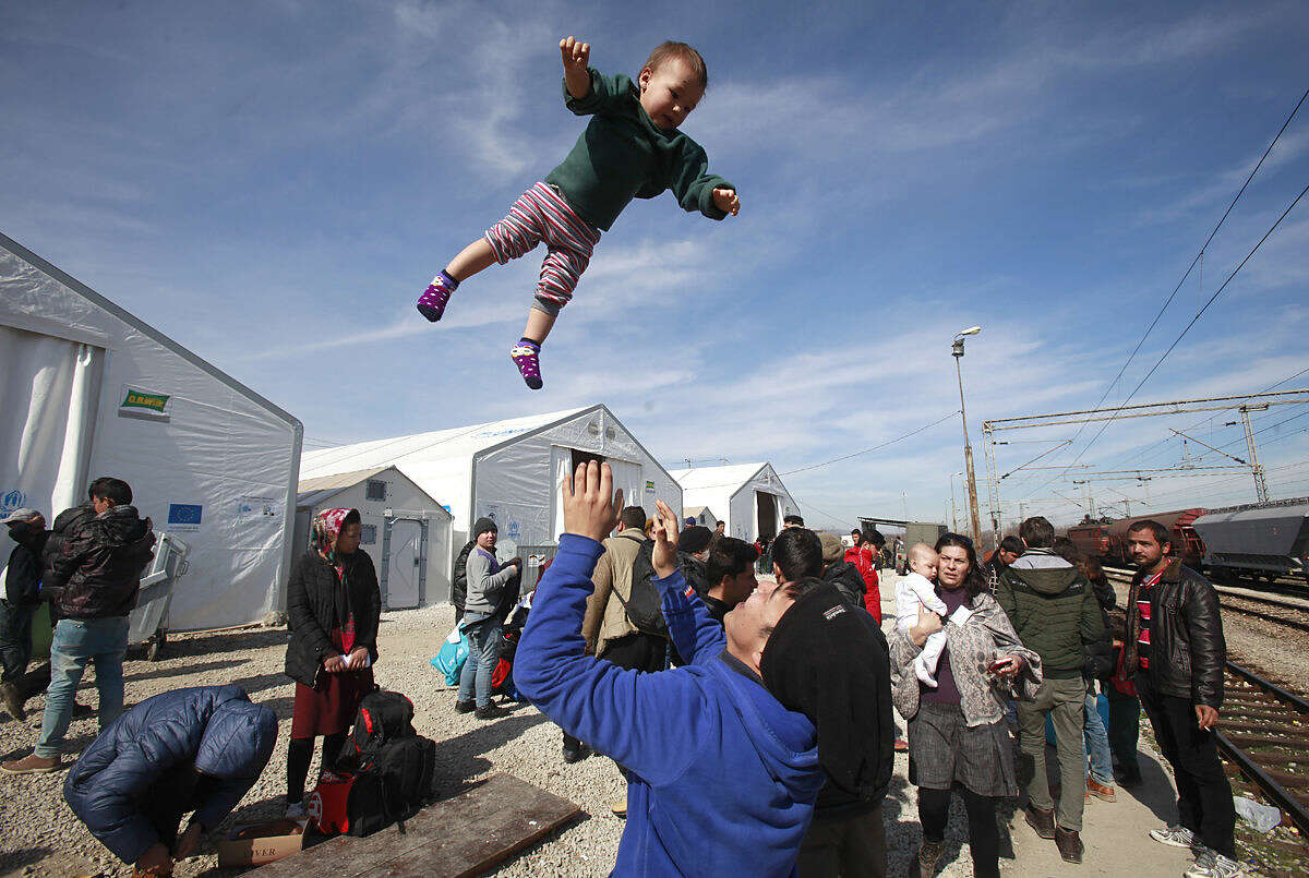 An Afghan refugee throws a child in the air at the transit center for refugees near the northern Macedonian village of Tabanovce, while waiting for a permission to cross the border into Serbia, Monday, Feb. 22, 2016. More than 600 Afghan refugees were stranded since Saturday at the transit center in Tabanovce in northern Macedonia. Serbia says the decision to block refugees from Afghanistan from passing through the so-called Balkan migrant corridor has been made by Austria and Slovenia. (AP Photo/Boris Grdanoski)