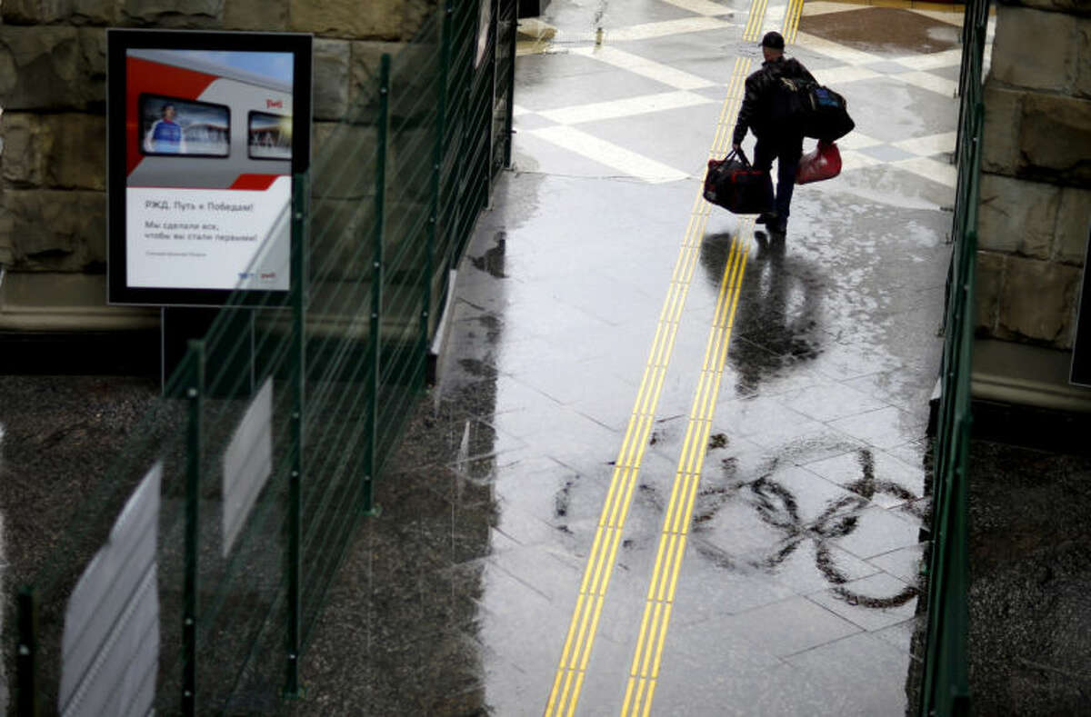 The Olympic rings are reflected in a puddle as a traveler carries bags out of the central train station, Wednesday, Jan. 29, 2014, in Sochi, Russia, home of the upcoming 2014 Winter Olympics. (AP Photo/David Goldman)