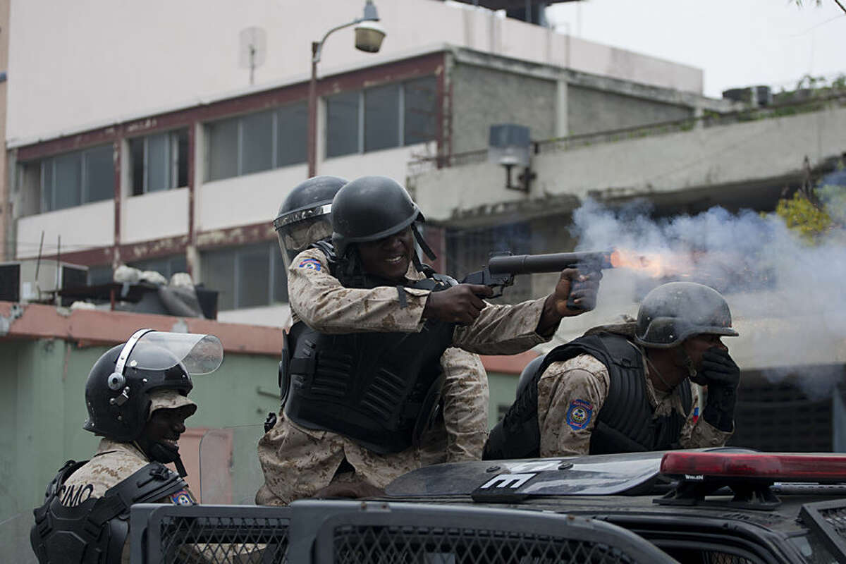 A national police officer fires a tear gas grenade towards protesters demanding that the government lower fuel prices, in Port-au-Prince, Haiti, Friday, Feb. 13, 2015. Students marched through Haiti's capital to demand lower gas prices and the ouster of President Michel Martelly. ( AP Photo/Dieu Nalio Chery)