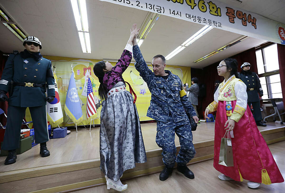 Graduate Park Jin, left, is congratulated by U.S. Navy LCDR Daniel E. "Dan-o" McShane of Charlotte, NC. after a graduation ceremony as South Korean border guard soldiers stand on the stage at the Tae Sung Dong Elementary School in Paju, South Korea, near Panmunjom inside the Demilitarized Zone separating South and North Korea, Friday, Feb. 13, 2015. The school is located just a few hundred meters from the fenced and mined border with North Korea. Four students graduated from the school Thursday. (AP Photo/Ahn Young-joon, Pool)