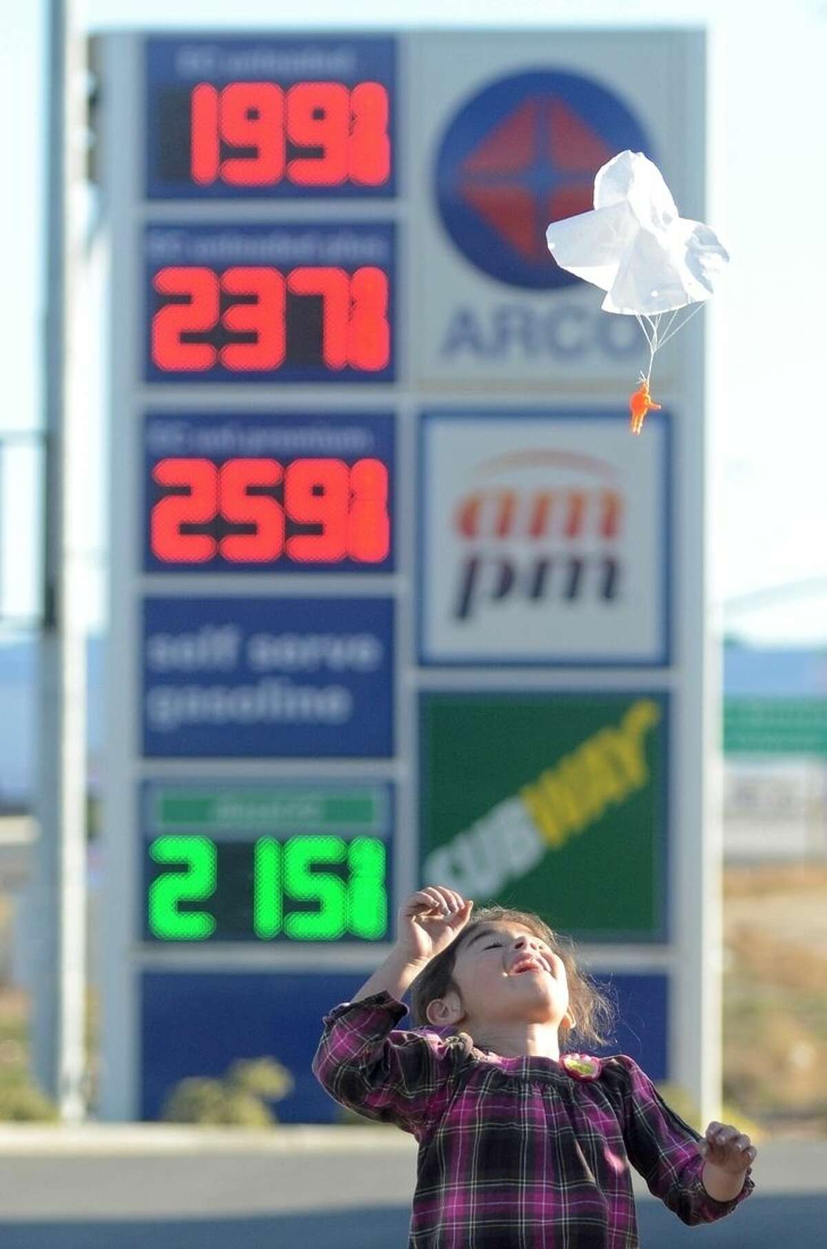 FILE - In this Wednesday, Feb. 24, 2016, file photo, Joanna Alvarez plays with a toy parachute man at an Arco gas station parking lot in Oak Hills, Calif. Gasoline prices are expected to keep rising until summer but remain far cheaper than recent years, due to the worldwide glut of oil. (David Pardo/Victor Valley Daily Press via AP, File)