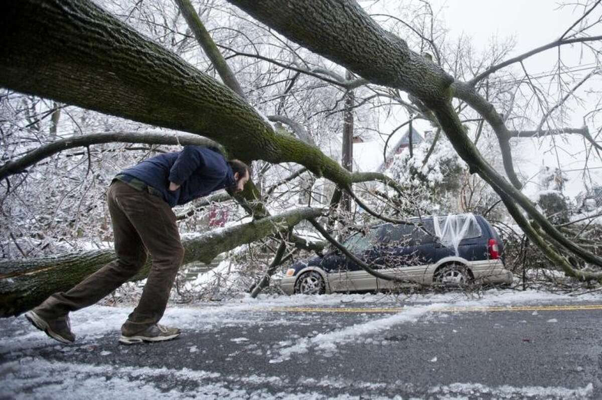 A man inspects an ice covered downed tree that took out an utility line and landed atop a minivan, after a winter storm Wednesday, Feb. 5, 2014, in Philadelphia. Icy conditions have knocked out power to more than 200,000 electric customers in southeastern Pennsylvania and prompted school and legislative delays as well as speed reductions on major roadways. (AP Photo/Matt Rourke)