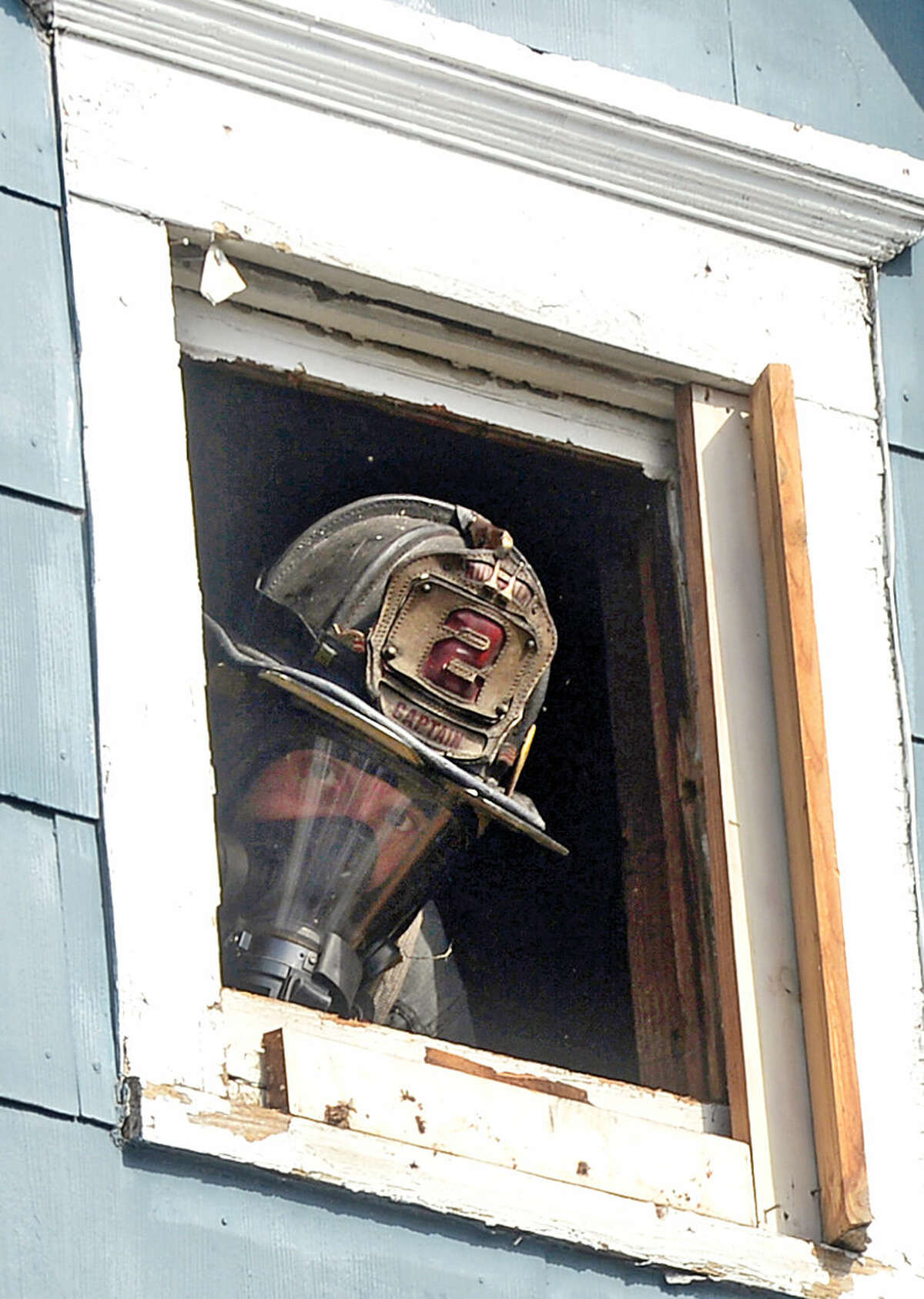 Hour photo / Erik Trautmann A Norwalk firefighter peers out of an attic window he vented while battling a fire that engulfed the rear deck of the home at 25 Leuvine Street in Norwalk Tuesday afternoon.