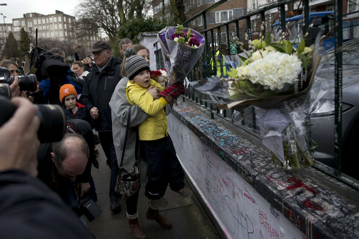 Tourists from Finland place flowers in memory of George Martin, the Beatles' producer, outside Abbey Road studios where the Beatles recorded albums and where the zebra crossing cover picture of the Abbey Road album was originally taken, in London, Wednesday, March 9, 2016. George Martin, the Beatles' urbane producer who quietly guided the band's swift, historic transformation from rowdy club act to musical and cultural revolutionaries, has died, his management said Wednesday March 9, 2016. He was 90. (AP Photo/Matt Dunham)
