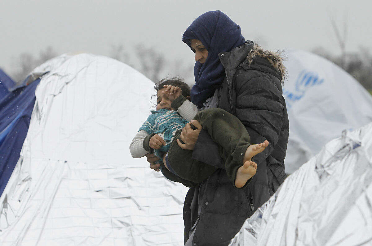 A Syrian refugee woman with a child walks in the rain among tents in an improvised camp on the border line between Macedonia and Serbia near the northern Macedonian village of Tabanovce, Thursday, March 10, 2016. Around 1.500 migrants and refugees are stranded at Tabanovce transit center for refugees in northern Macedonia. (AP Photo/Boris Grdanoski)