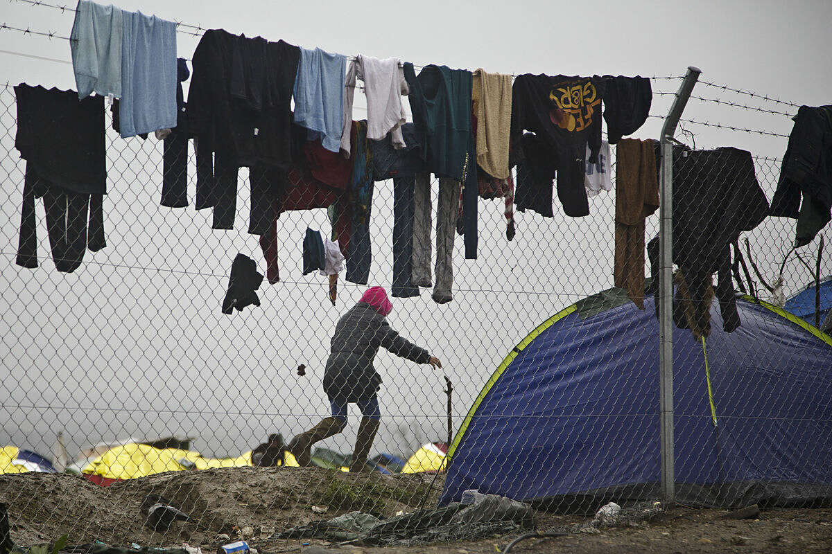 Migrant runs among clothes hanged to dry on a fence at the Greek border camp near Idomeni, Thursday, March 10, 2016. After nearly three days of rain, conditions in the refugee camp on the Greek-Macedonian where about 14,000 people are stranded have deteriorated significantly, with many of its residents struggling to re-pitch their small camping tents in slightly drier patches. (AP Photo/Visar Kryeziu)