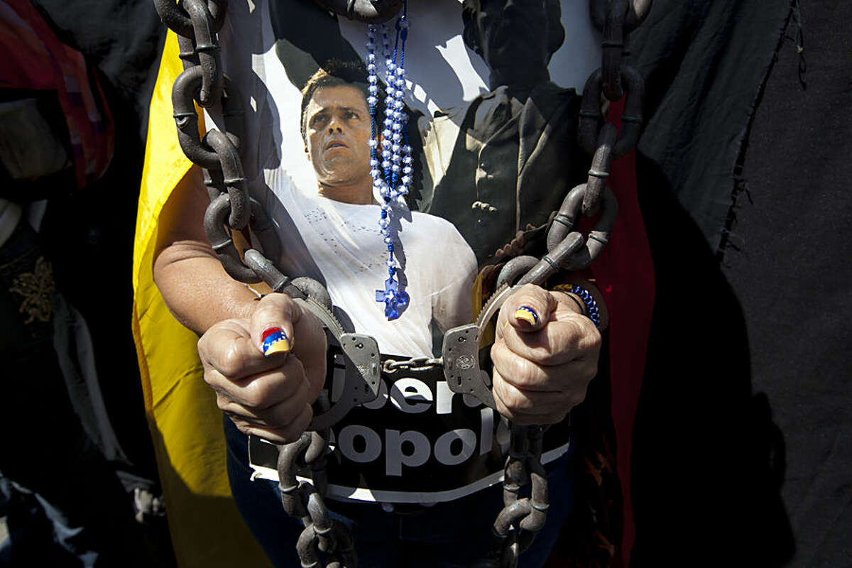 A woman wearing handcuffs, chains and a rosary holds a poster of jailed opposition leader Leopoldo Lopez at an event marking the one year anniversary of his arrest and imprisonment in Caracas, Venezuela, Wednesday, Feb. 18, 2015. One year has passed since Venezuela's streets were rocked by anti-government protests that left 43 people dead and neighborhoods disrupted by flaming barricades. The unrest culminated with the arrest of Lopez, a former Caracas-area mayor and key opposition leader. (AP Photo/Ariana Cubillos)