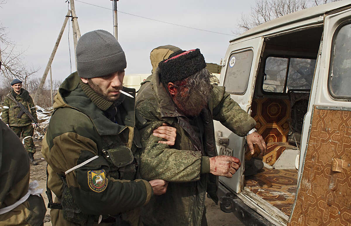 A wounded Cossack is carried away by fellow fighters after his car hit a land mine in the east Ukraine town of Debaltseve on Thursday, Feb. 19, 2015. After weeks of relentless fighting, the embattled Ukrainian rail hub of Debaltseve fell Wednesday to Russia-backed separatists, who hoisted a flag in triumph over the town. The Ukrainian president confirmed that he had ordered troops to pull out and the rebels reported taking hundreds of soldiers captive. (AP Photo/ Peter Leonard)