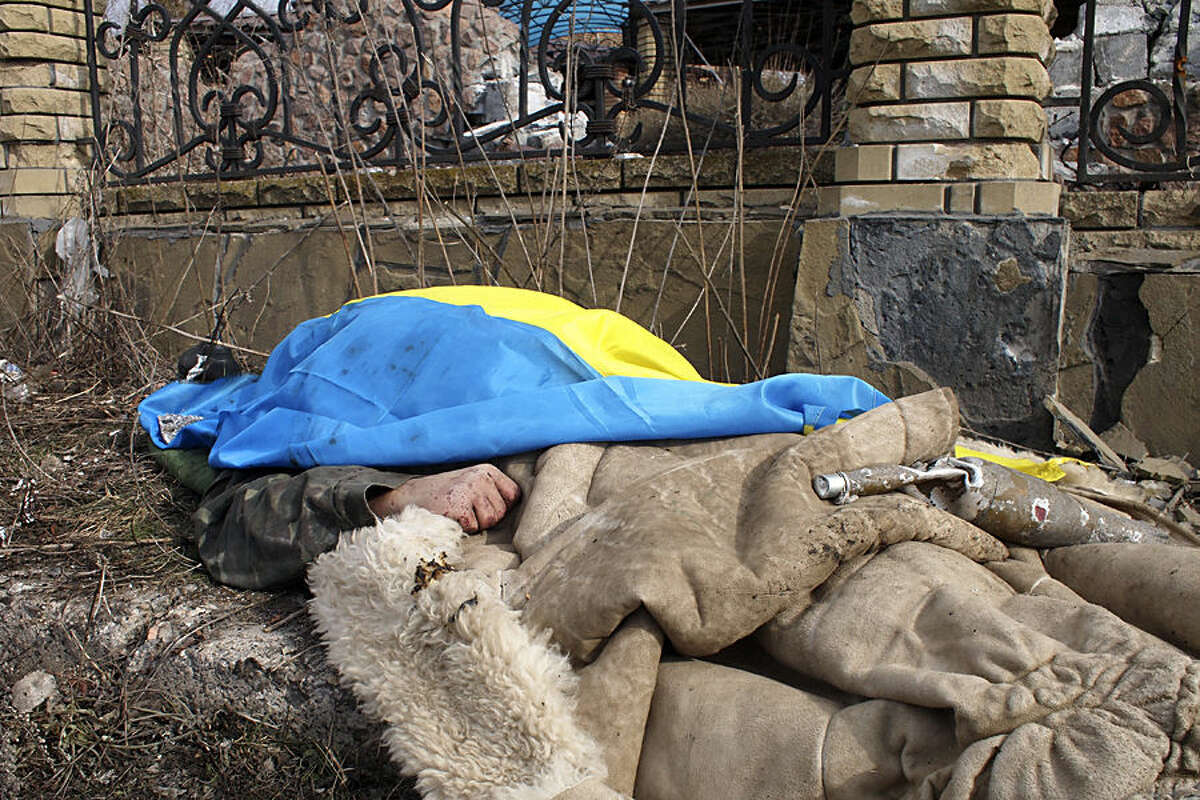 A body of a government soldier lies by the side of the road and is covered by a Ukrainian national flag in the east Ukraine town of Debaltseve on Thursday, Feb. 19, 2015. After weeks of relentless fighting, the embattled Ukrainian rail hub of Debaltseve fell Wednesday to Russia-backed separatists, who hoisted a flag in triumph over the town. The Ukrainian president confirmed that he had ordered troops to pull out and the rebels reported taking hundreds of soldiers captive. (AP Photo/ Peter Leonard)